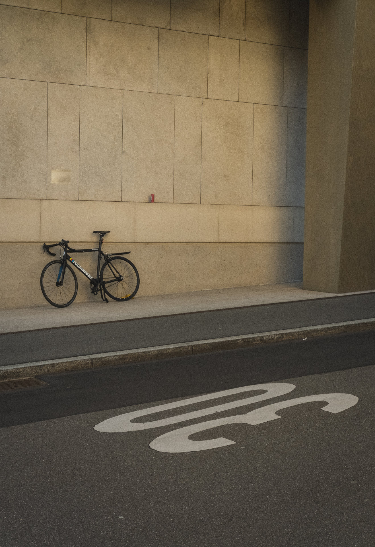 Eenzame fiets tegen een grote stenen gevel in zacht licht.