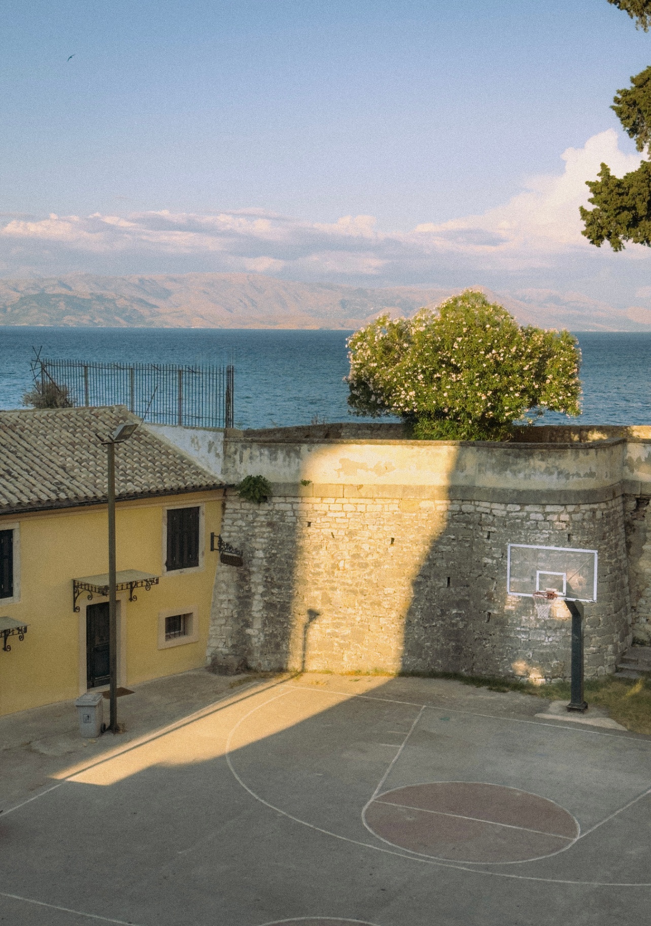 Basketbalveld bij een geel huis met uitzicht over de zee in Corfu.