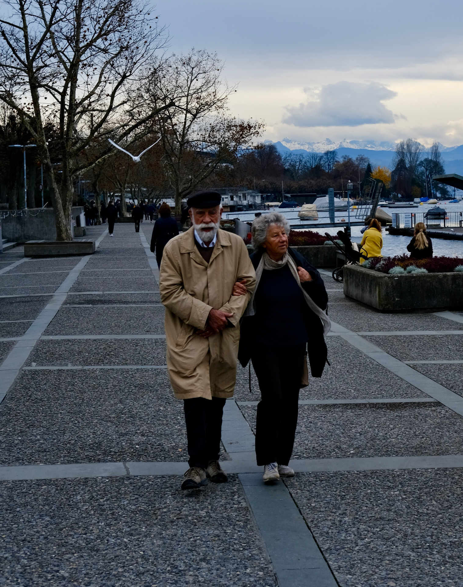 Ouder stel wandelt langs het water met bergen op de achtergrond.