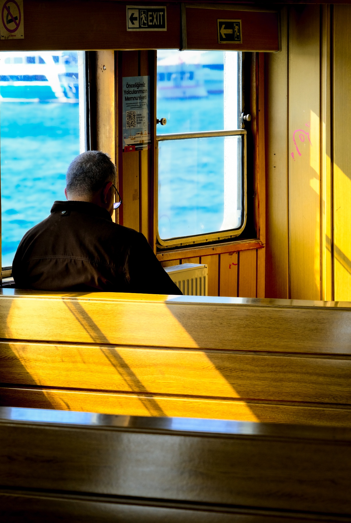 Man zit binnen op een veerboot terwijl zonlicht over houten banken valt.