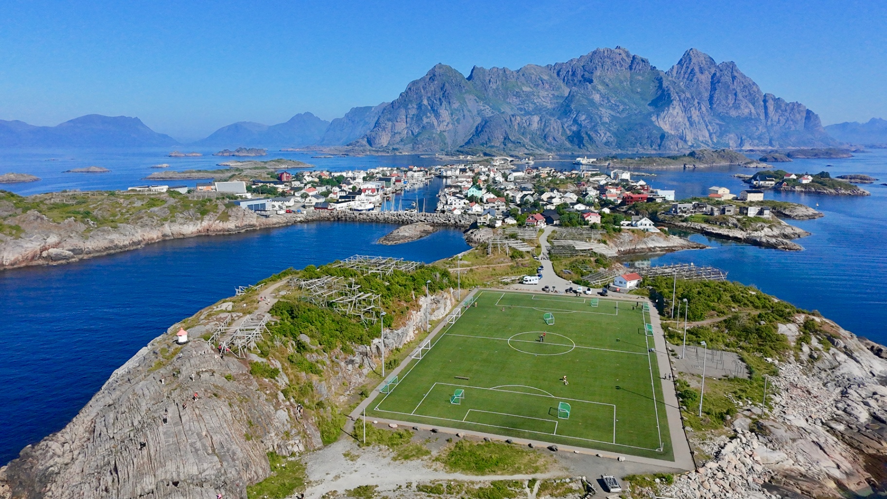 Luchtfoto van een voetbalveld op een rotseiland in de Lofoten, omringd door fjorden en bergen.