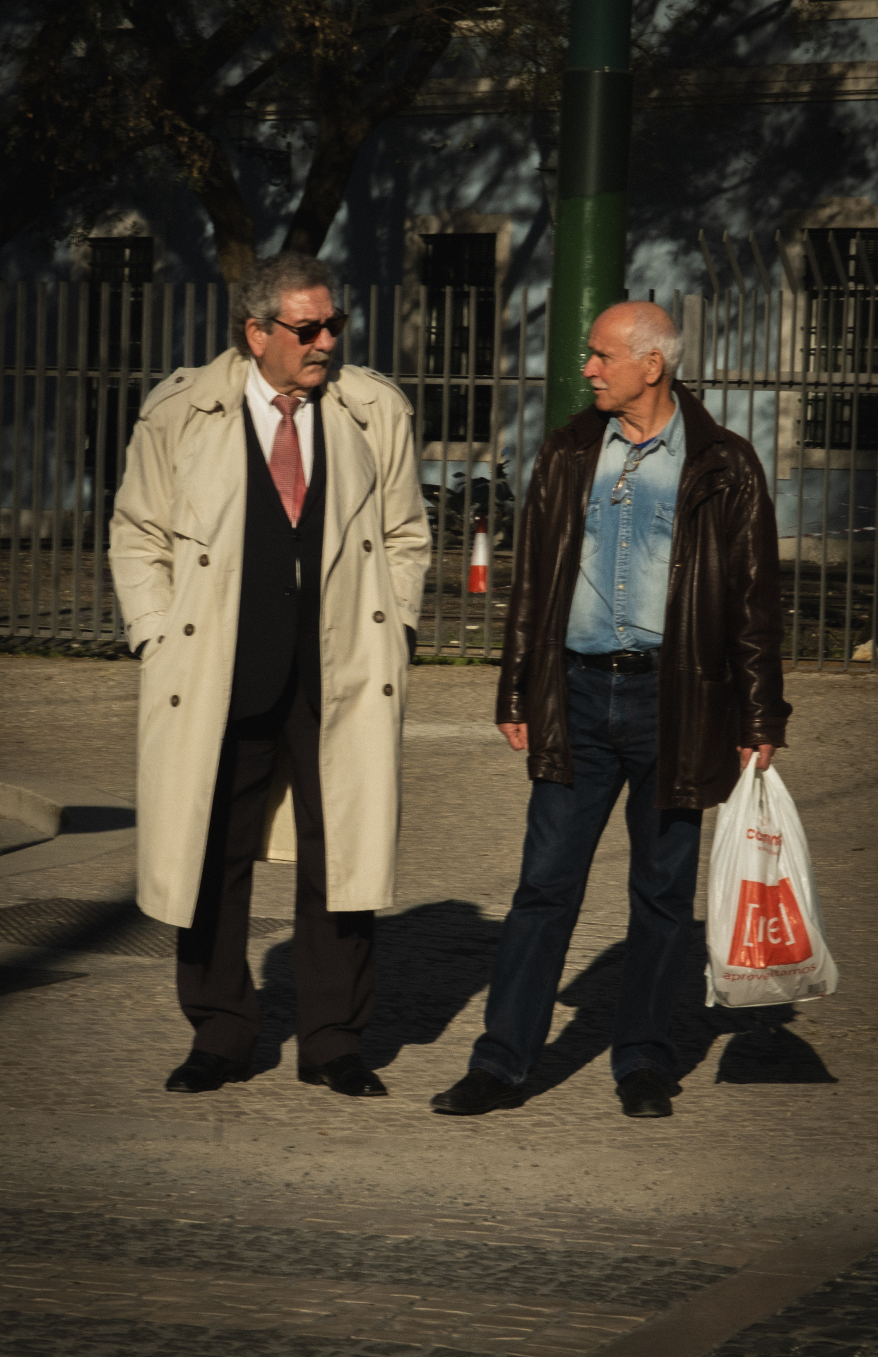Twee oudere mannen in gesprek op straat in warm middaglicht.