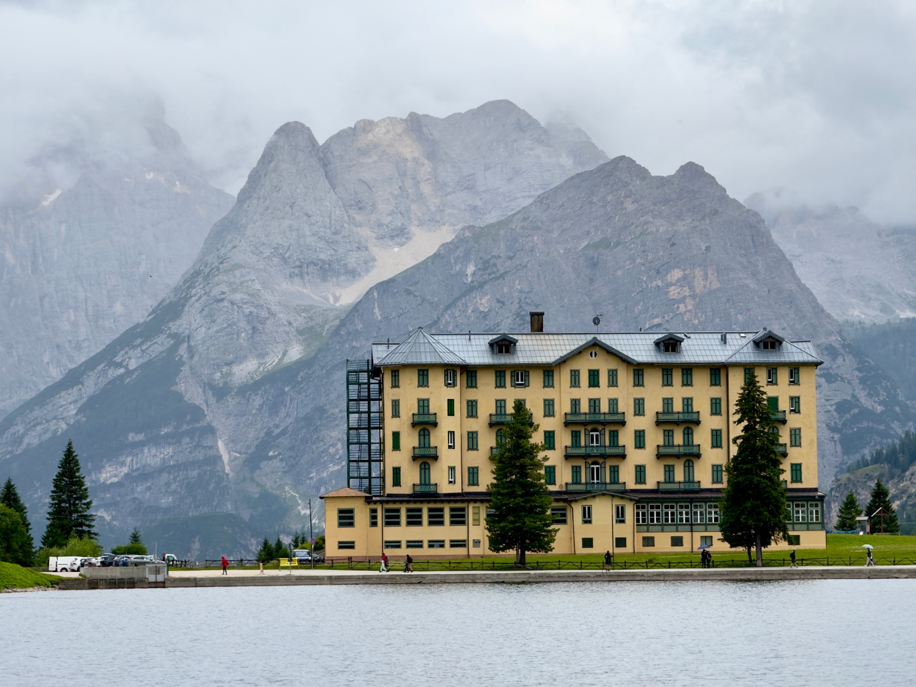 Geel hotel aan een meer in de Dolomieten met bergen in de wolken.