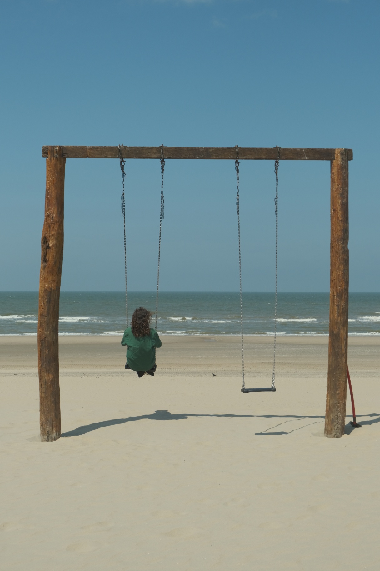 Persoon op een houten schommel kijkt uit over een leeg strand en de zee.