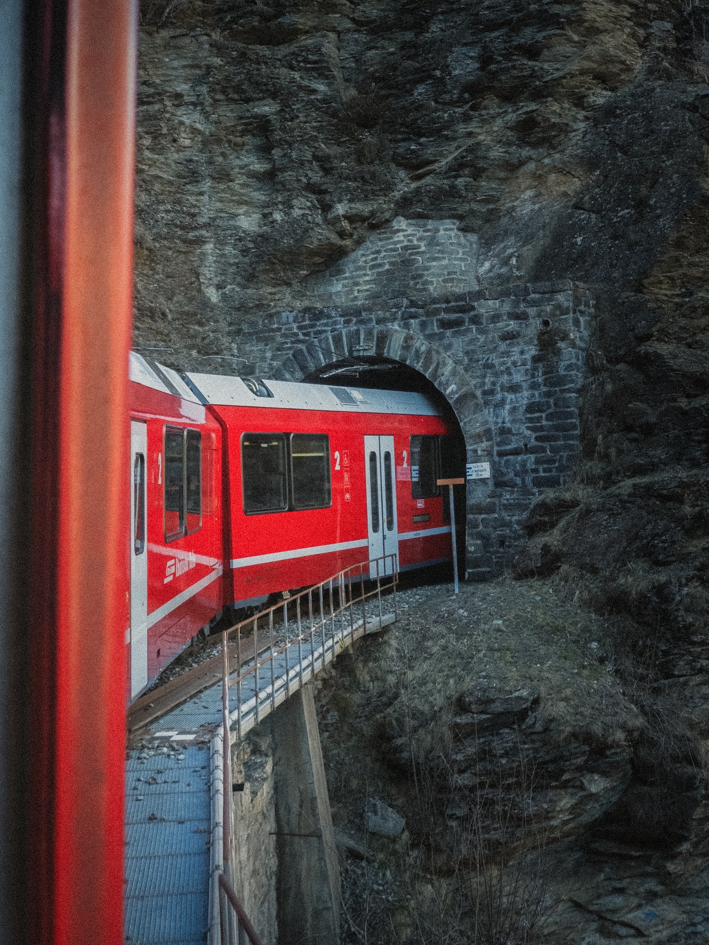 Rode trein die een donkere tunnel in rijdt tussen de rotsen.